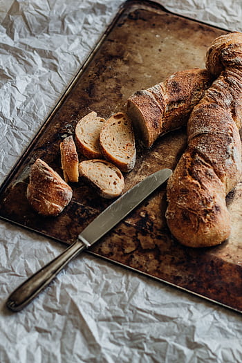Freshly baked rustic bread loaf with slices on a textured baking tray. HD phone wallpaper