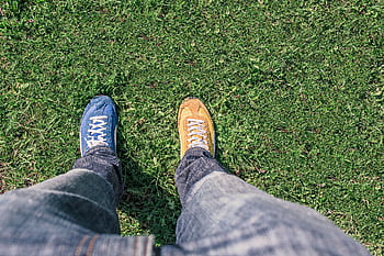 A person wearing mismatched shoes stands on green grass, highlighting differences and individuality. HD wallpaper