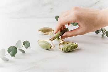 Close-up of a hand holding jade rollers on a marble surface for skincare and wellness. HD wallpaper