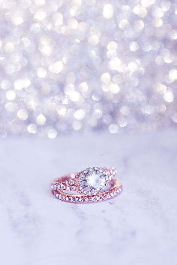 Close-up of a sparkling diamond engagement ring on a marble surface with bokeh background. HD phone wallpaper