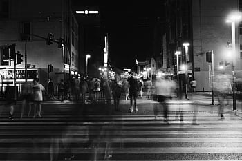 A bustling nighttime city scene with blurred pedestrians crossing a street under urban lights. HD wallpaper