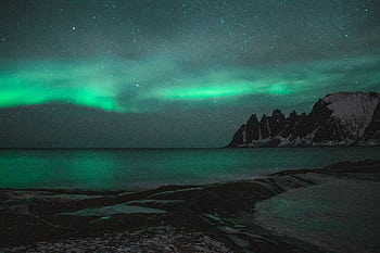 Breathtaking view of aurora borealis over calm sea and mountains under a starry sky. HD wallpaper