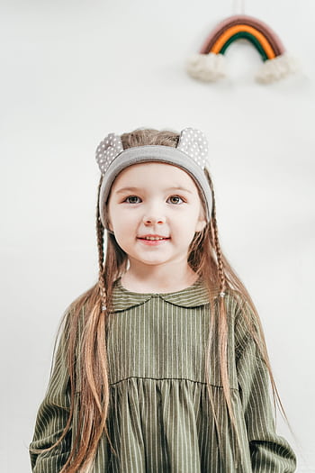 Charming portrait of a young girl in a green dress with a cute headband, smiling indoors. HD phone wallpaper