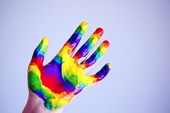 A vibrant hand covered in rainbow paint against a plain background, symbolizing creativity. HD wallpaper