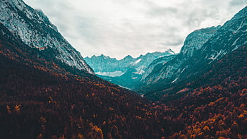 Discover the stunning autumn colors in this serene mountain valley landscape, captured with dramatic cloudy skies. HD wallpaper