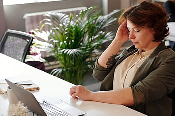 A businesswoman feeling stressed at her home office desk while working on her laptop. HD wallpaper