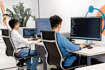 Two male developers at desks programming in a modern office workspace with large monitors. HD wallpaper