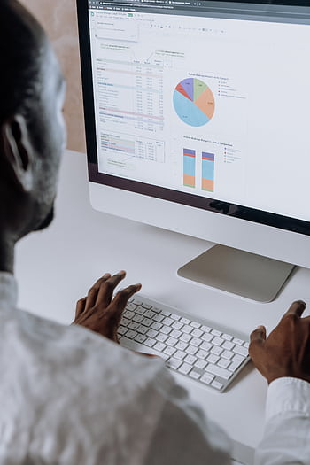 Businessman analyzing charts and data on computer in office setting. HD phone wallpaper
