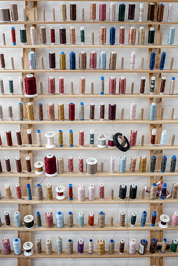 A vibrant array of thread spools neatly arranged on a wooden display shelf. HD phone wallpaper