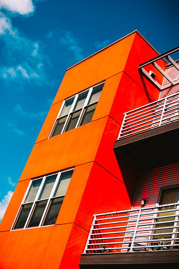 Low angle of a vibrant orange modern apartment building against a bright blue sky in Eau Claire. HD phone wallpaper