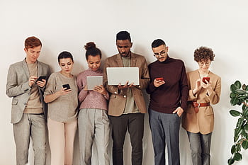 A diverse group of adults interacting with various devices in a stylish office setting, showcasing modern technology use. HD wallpaper