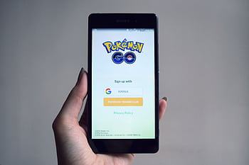 Smart displaying Pokémon Go app sign-in screen, held in hand. HD wallpaper