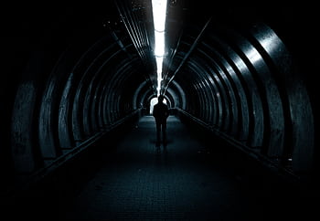 A lone figure stands in a dimly lit tunnel, creating an air of mystery. HD wallpaper