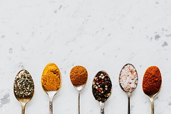 A variety of colorful spices and seasonings on six spoons arranged on a marble surface. HD wallpaper