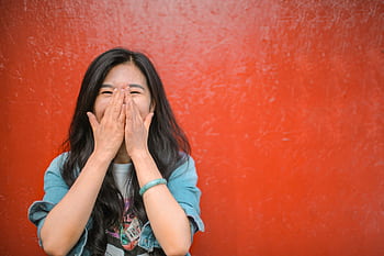 Portrait of a cheerful young woman covering her face with delight against a vibrant red background. HD wallpaper