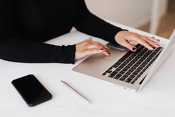 Professional woman typing on a laptop with smart and pen on desk, emphasizing modern business lifestyle. HD wallpaper