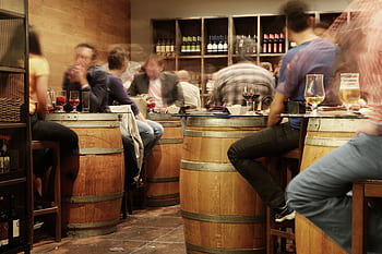Lively bar setting with people enjoying drinks and tapas around wine barrel tables. HD wallpaper
