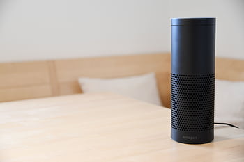 A black smart speaker resting on a light-colored wooden table in a cozy indoor setting. HD wallpaper