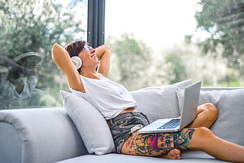 Woman reclining on a couch, using laptop while listening to music with heads, smiling and relaxed. HD wallpaper