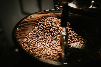Close-up of freshly roasted coffee beans in a large industrial coffee roaster, showcasing rich textures and warm tones. HD wallpaper