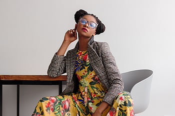 Elegant woman posing in a modern setting, wearing a floral dress and eyeglasses. HD wallpaper