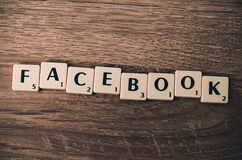 Scrabble tiles spelling 'Facebook' on a wood background, symbolizing social media. HD wallpaper