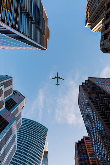 Airplane flies over Chicago's modern skyscrapers against a clear sky, highlighting urban architecture. HD phone wallpaper
