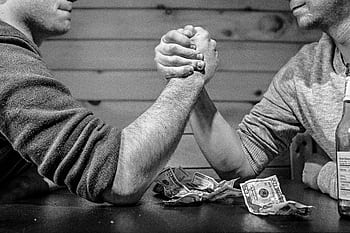 Two men engage in a high-stakes arm wrestling match surrounded by money on a table. HD wallpaper