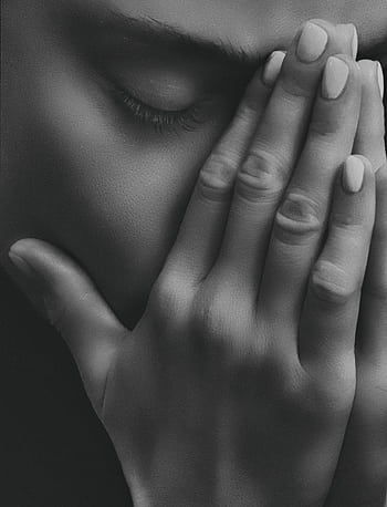 Black and white close-up of a person's face with hands clasped in distress, conveying strong emotions. HD phone wallpaper