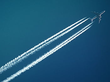 Aerial view of an airplane in flight, leaving vapor trails against a clear blue sky. HD wallpaper