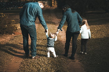 A family of four walks hand in hand on a path, enjoying a sunny day outdoors. HD wallpaper