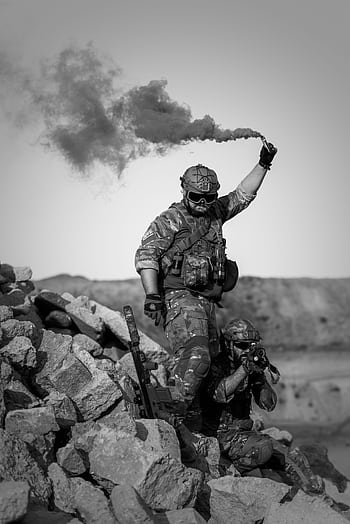 Two soldiers in action with smoke signal in rocky desert terrain. HD phone wallpaper