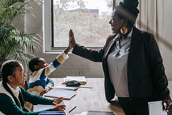 Teacher and students share a high five, fostering teamwork and learning in a classroom setting. HD wallpaper