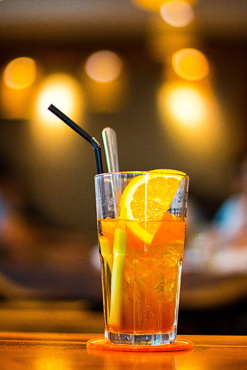 A vibrant orange iced tea garnished with fresh citrus slices in a lively indoor setting. HD phone wallpaper