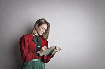 Elegant woman in glasses writing notes with a book in hand indoors. HD wallpaper