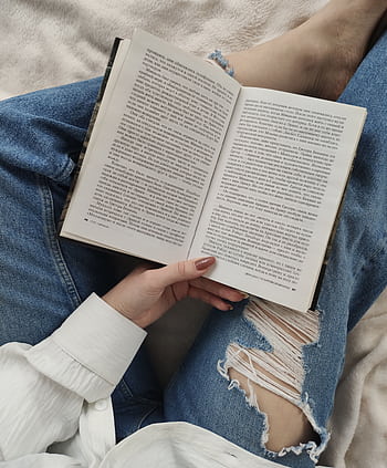 A woman enjoys a relaxing day reading a book while lounging indoors, dressed in casual jeans. HD phone wallpaper