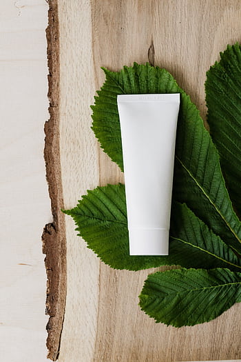 Minimalist white cosmetic tube on lush green leaves for skincare mockup. HD phone wallpaper