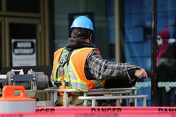 A construction worker wearing a blue helmet and safety vest operates equipment at an urban construction site. HD wallpaper