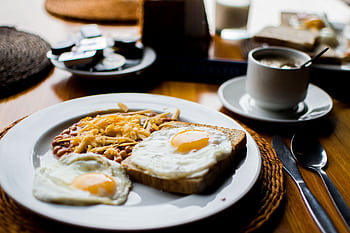 A hearty breakfast with fried eggs, baked beans, and toast served with coffee in a cozy setting. HD wallpaper