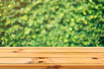 A wooden table surface with a vibrant green garden background in soft focus. HD wallpaper