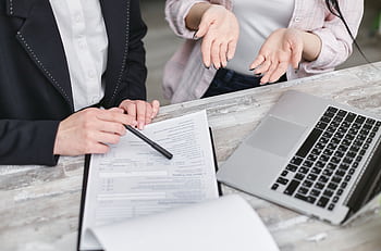 Two professionals discussing a contract at a business meeting with documents and a laptop. HD wallpaper
