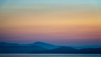 A tranquil landscape scene capturing a sunset over misty mountains and calm sea. HD wallpaper