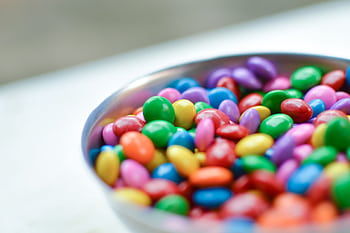 Vibrant close-up of assorted candy-coated chocolates in a silver bowl. HD wallpaper
