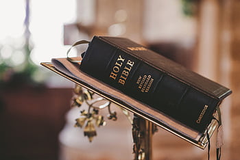 Holy Bible open on a stand inside a church, symbolizing faith and spirituality. HD wallpaper