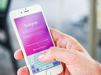 Close-up of a hand holding a smart displaying the Instagram login screen, highlighting mobile technology. HD wallpaper