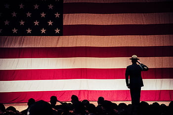 A solemn moment as a soldier salutes the American flag during a ceremony inside an auditorium. HD wallpaper