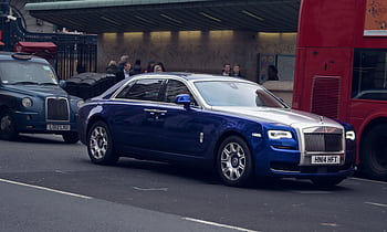 A blue luxury car driving on a busy street in London, surrounded by iconic vehicles. HD wallpaper
