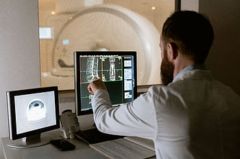 Medical professional reviewing MRI scans on computer screens for diagnostic purposes. HD wallpaper