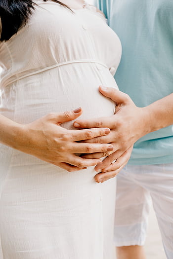 Close-up of hands gently embracing a baby bump in a warm, serene setting. HD phone wallpaper