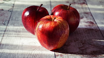 Close-up of fresh red apples on a rustic wooden table captured in natural light. HD wallpaper
